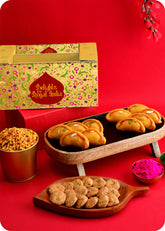 A Holi gift pack featuring traditional Indian sweets including Shahi Gujiya, Khatta Meetha Mix, Methi Swali and herbal gulal.