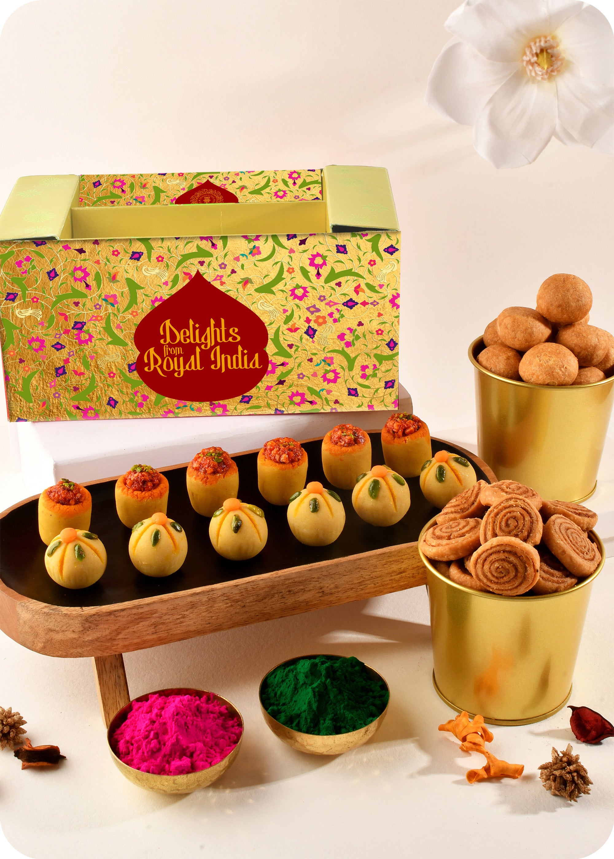 A colorful presentation of Holi sweets including Thandai Laddoo, Pan Laddoo, Kachori, and Bhakarwadi, and herbal gulal.
