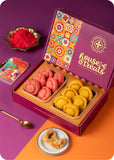 A gift box of Holi sweets containing rose and saffron colored Chandrakala sweets, along with herbal Gulal.