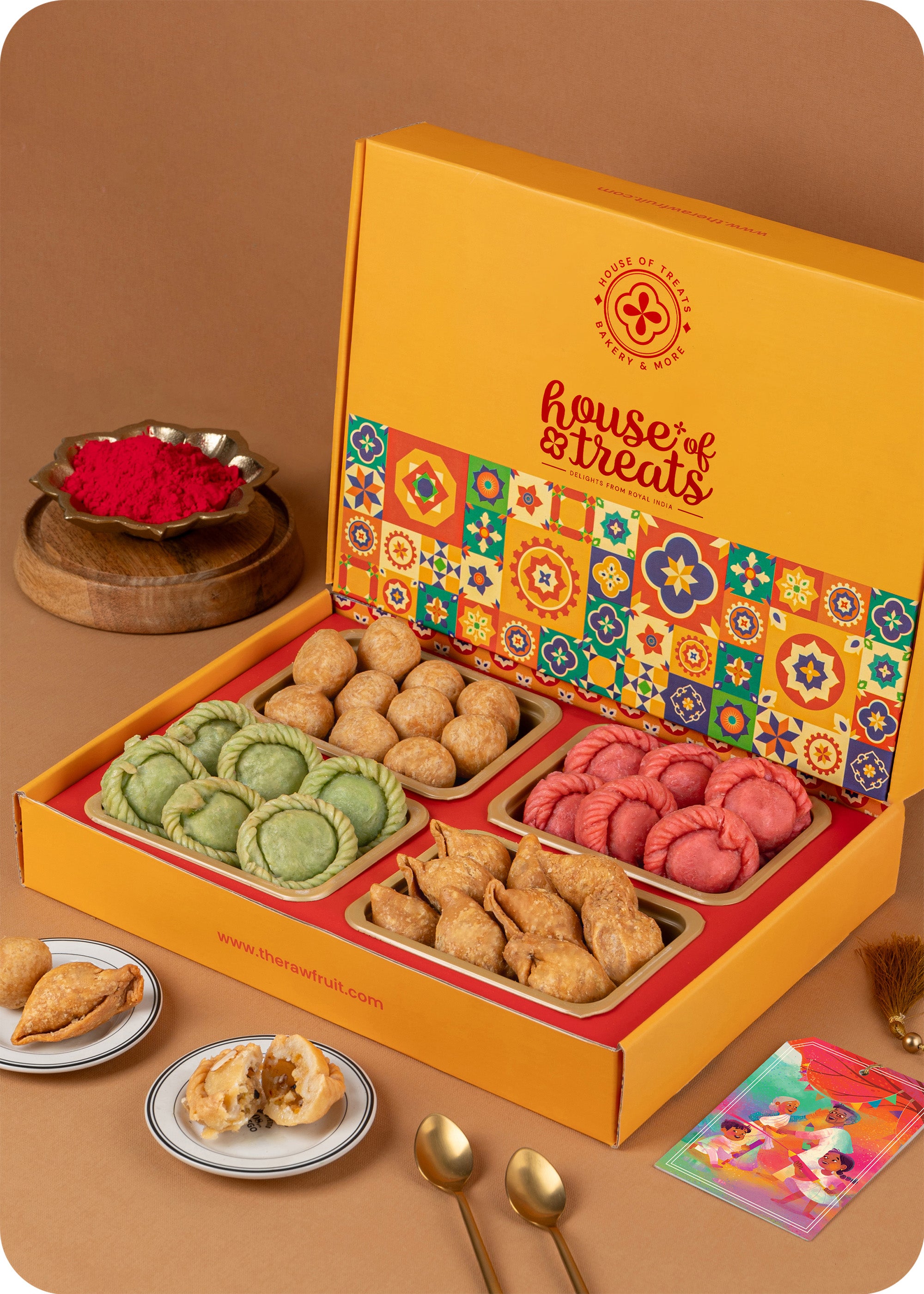 A colorful Holi Gift Pack from The House Of Treats containing various traditional Indian snacks such as Pista & Rose Chandrakala, Samosa, and Kachori and herbal gulal.