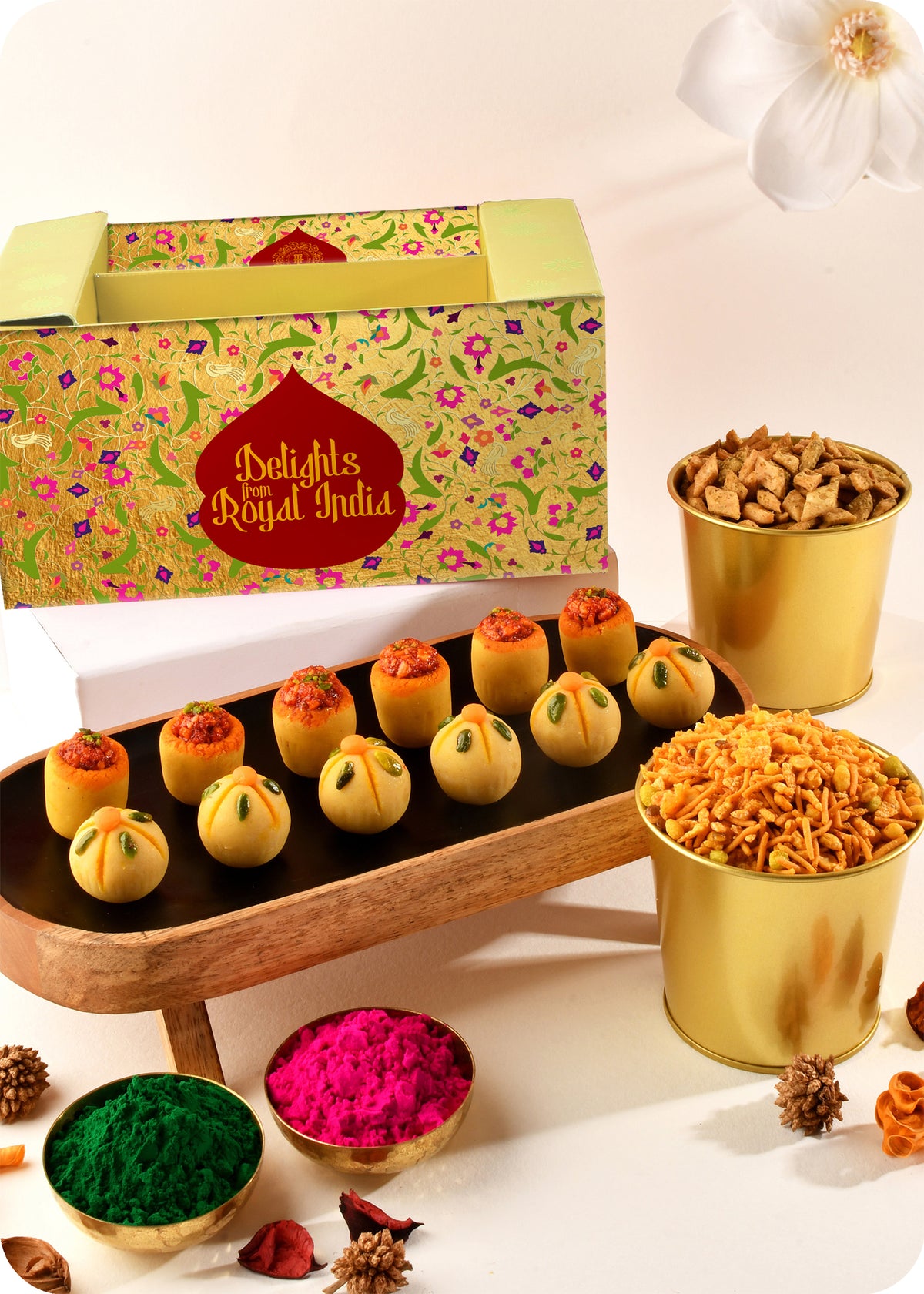 A Holi gift pack featuring an assortment of sweets including Thandai Laddoo, Pan Laddoo, Pudhina Paare, and Khatta Meetha Mix and herbal gulal.