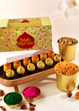 A Holi gift pack featuring an assortment of sweets including Thandai Laddoo, Pan Laddoo, Pudhina Paare, and Khatta Meetha Mix and herbal gulal.