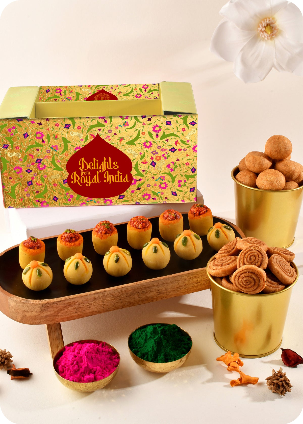 A colorful presentation of Holi sweets including Thandai Laddoo, Pan Laddoo, Kachori, and Bhakarwadi, and herbal gulal.