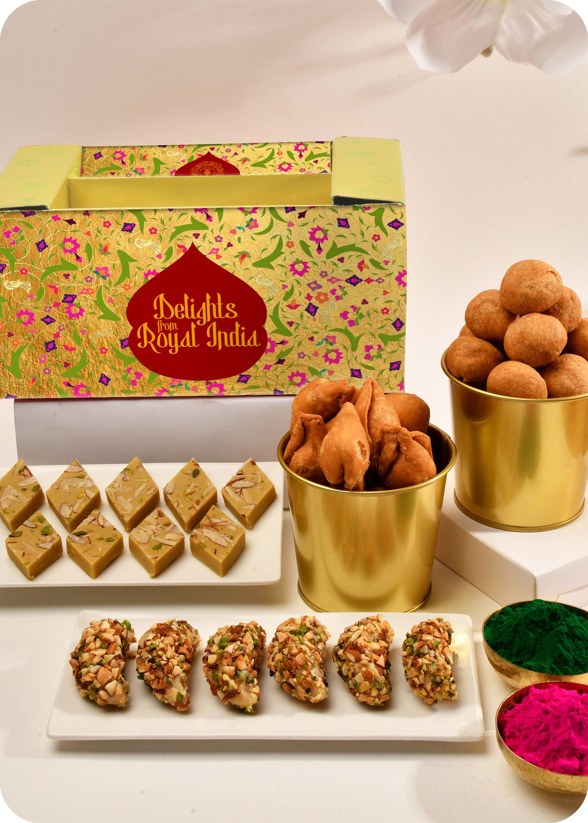 A Holi gift pack featuring an assortment of dry fruit gujiya, thandai katli, kachori, and samosa, and herbal gulal.