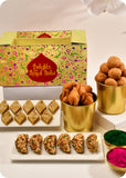 A Holi gift pack featuring an assortment of dry fruit gujiya, thandai katli, kachori, and samosa, and herbal gulal.