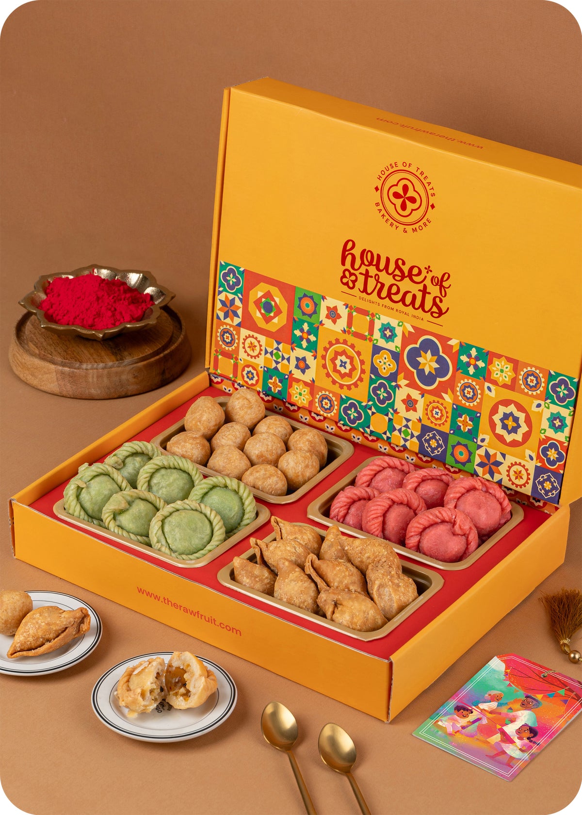 A colorful Holi Gift Pack from The House Of Treats containing various traditional Indian snacks such as Pista & Rose Chandrakala, Samosa, and Kachori and herbal gulal.